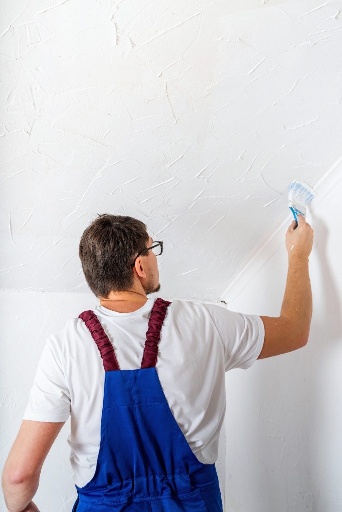 Man in blue overall painting wall with paintbrush